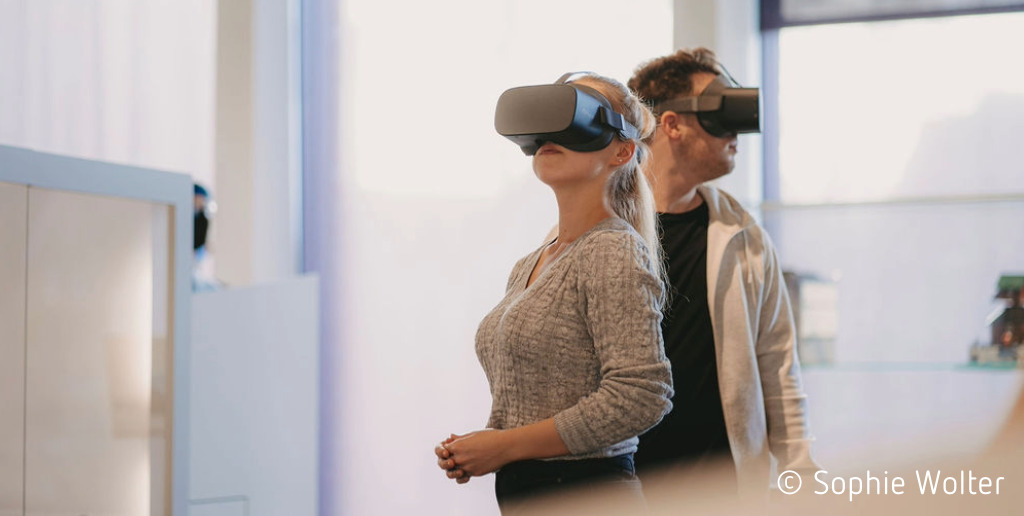 Eine Besucherin und ein Besucher stehen in der Ausstellung im Museum Lüneburg, tragen VR-Brillen und schauen sich im virtuellen Raum um.