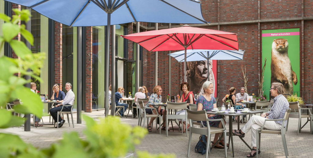 Terrasse des Museums an der Ilmenau mit Sonnenschirmen und vielen Café-Gästen.