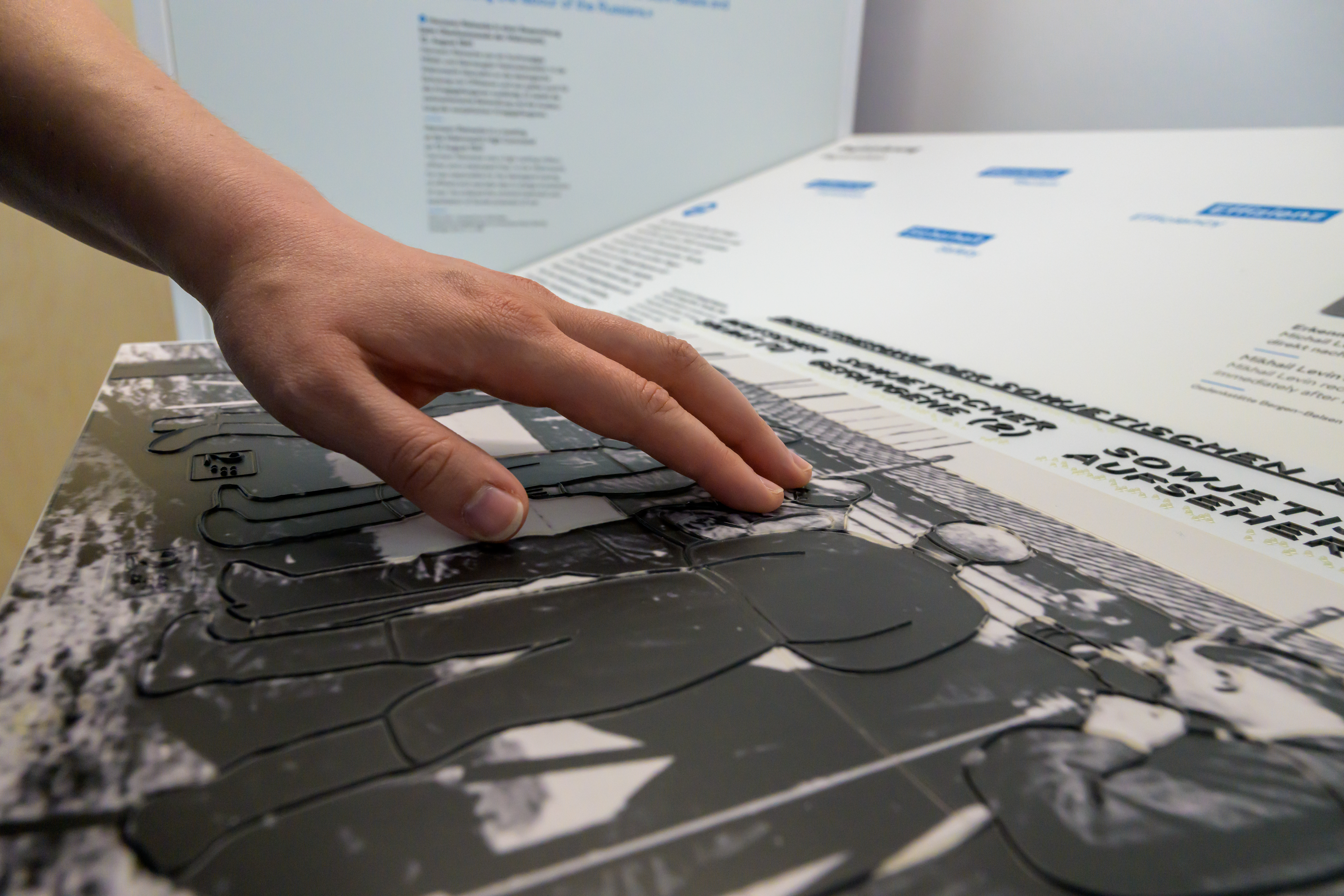 Ausstellung "Ein Tatort: Bergen-Belsen" in der Gedenkstätte Bergen-Belsen: eine Hand fährt über die taktilen Elemente einer Ausstellungstafel.
