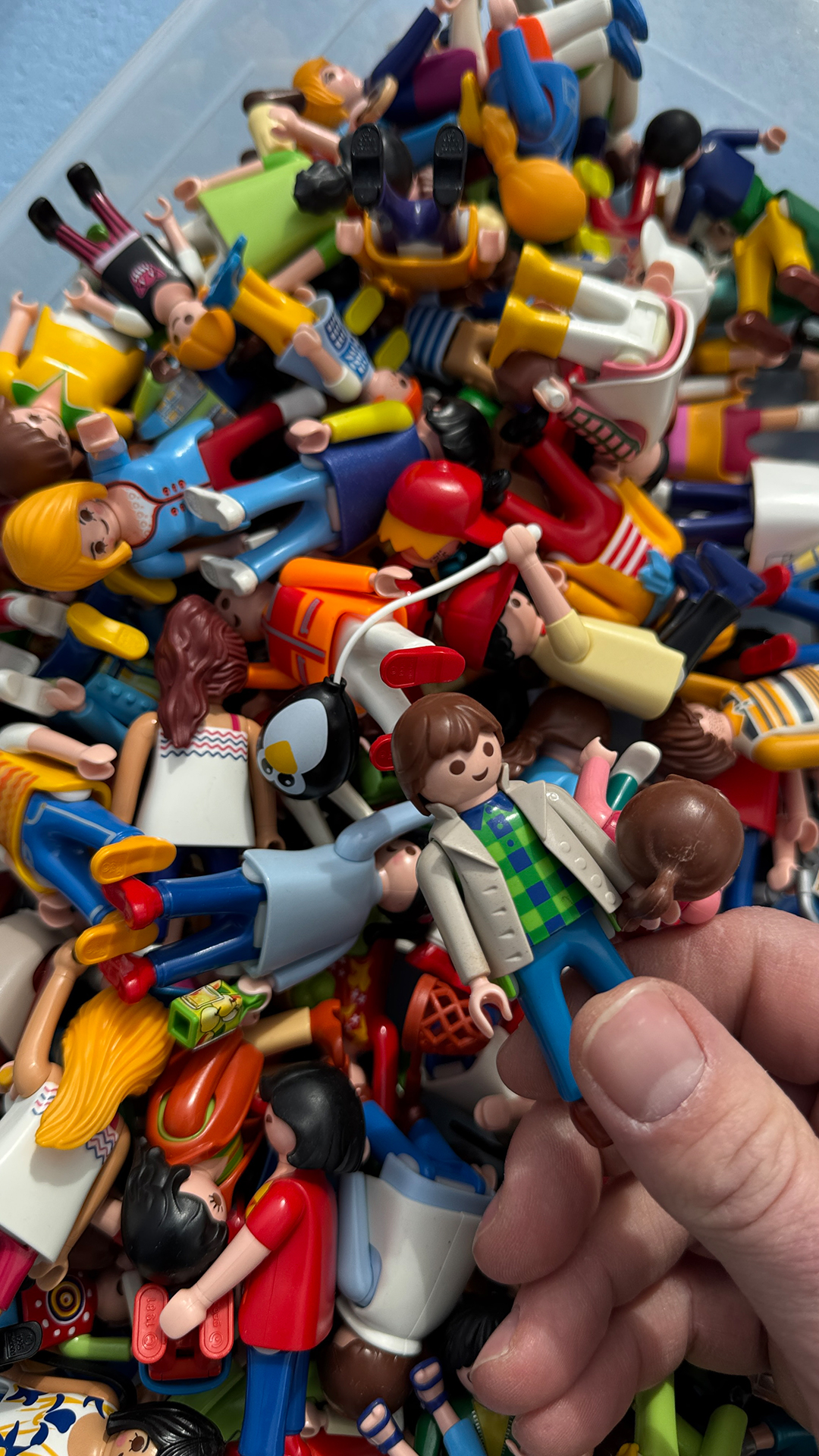 Eine Hand greift in eine Kiste voll mit bunten PLAYMOBIL-Figuren