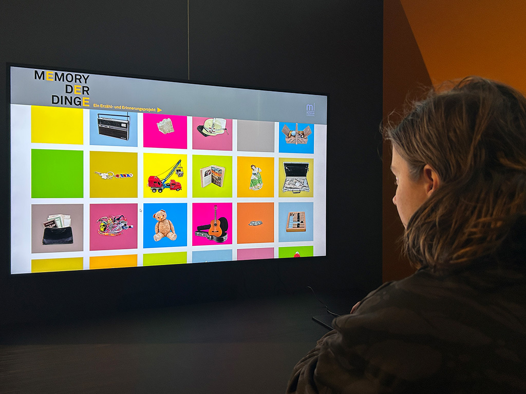 Eine Person sitzt vor dem Bildschirm der Medienstation "Memory der Dinge" im Museum Lüneburg und scrollt durch die verschiedenen Objekte.