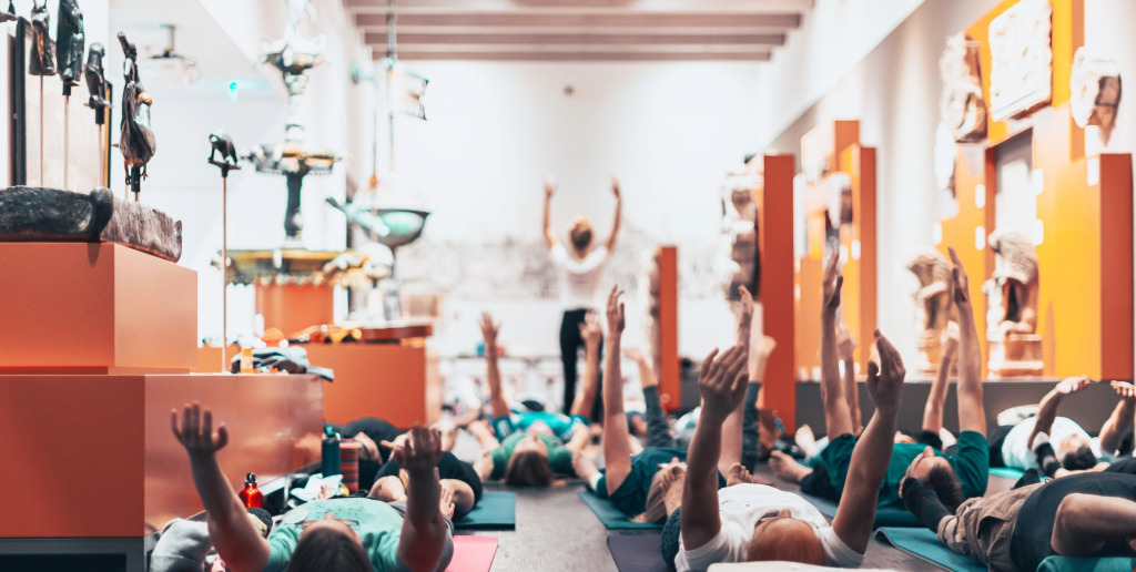 Yoga im Museum Menschen liegen beim Yoga im Museum mit dem Rücken auf Yoga-Matten in der Ausstellung zwischen den Exponaten und strecken ihre Hände in die Höhe.